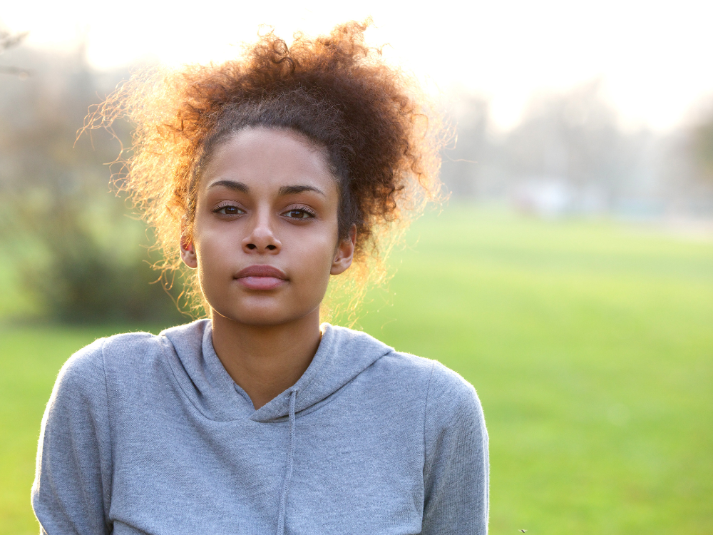 A young Black woman wearing a grey hoodie looks at the camera