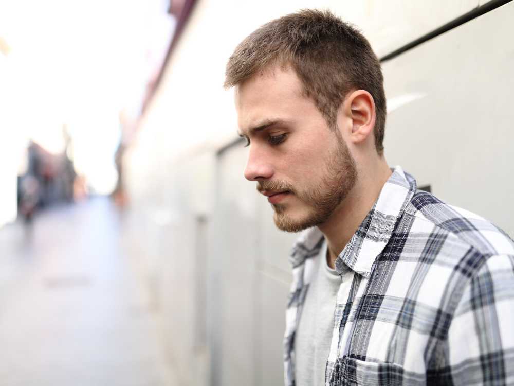A young white man with short brown hair and beard looking at the ground.