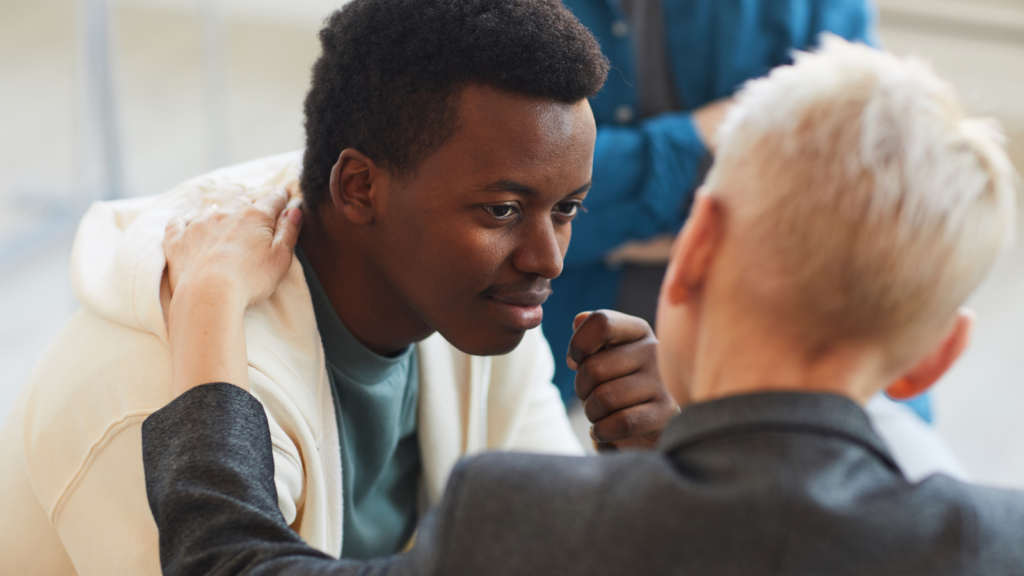 A young Black man smiles at a white person with short blond hair whose face we cannot see