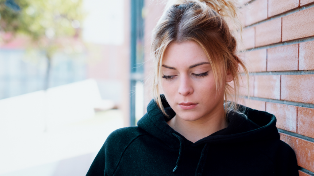 A young white woman wearing a black hoodie looks at the ground