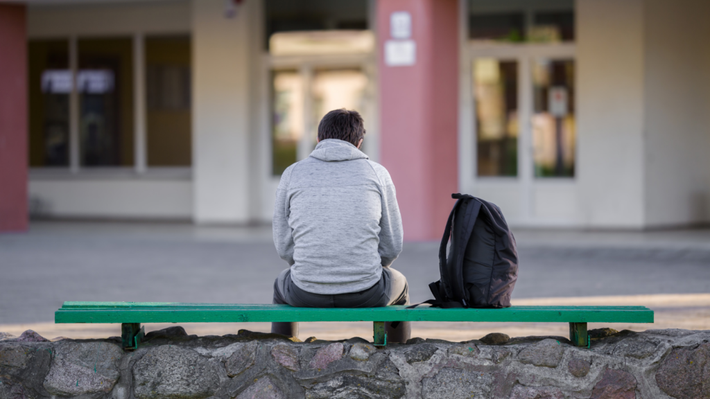 Young man sitting down on bench with back to camera