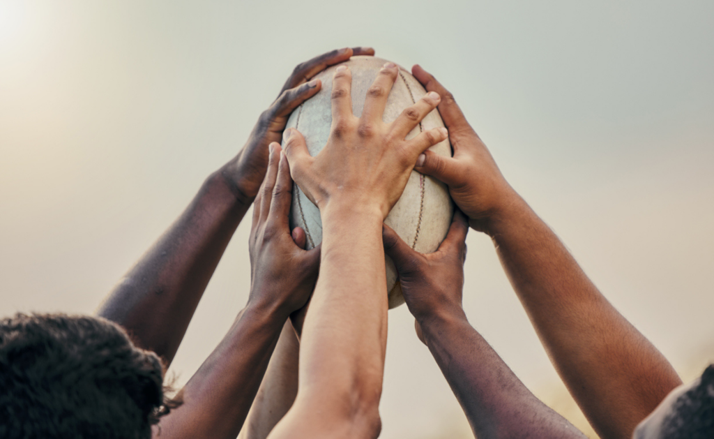 Many hands reaching for a rugby ball in the air